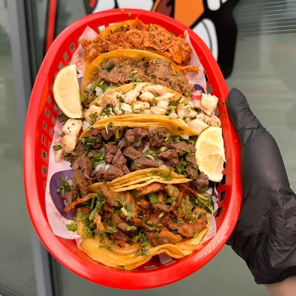 A red basket holds six Space City Birria tacos with various fillings and lime wedges.