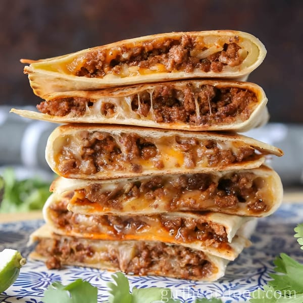 Stack of five Space City Birria quesadillas, filled with meat and melted cheese, on a patterned plate.