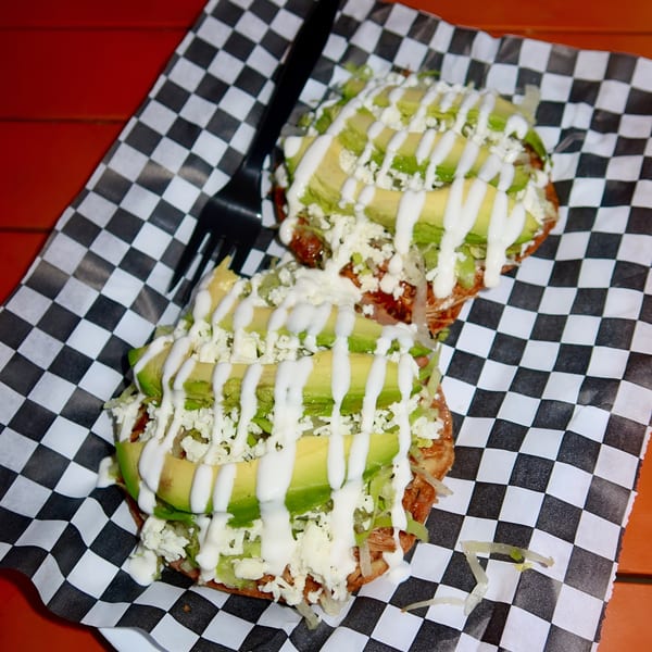 Two Space City Birria tostadas topped with avocado, cheese, and crema on checkered paper.